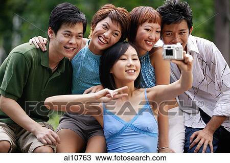 Stock Image - Friends sitting side by side, posing for camera. Fotosearch