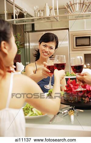 Friends toasting wine glasses across dinner table, over the shoulder view View Large Photo Image Stock Photo - Friends toasting wine glasses across dinner table, over the shoulder view. Fotosearch