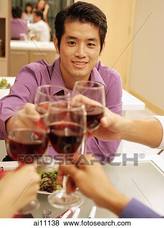 Friends toasting wine glasses across dinner table, over the shoulder view View Large Photo Image Stock Photo - Friends toasting wine glasses across dinner table, over the shoulder view. Fotosearch