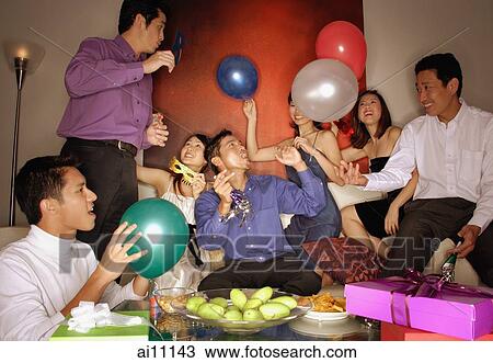 Stock Image - Group of friends having a party at home, holding balloons. Fotosearch