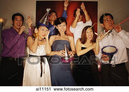 Stock Image - Group of friends having a party at home, playing with streamers and noisemakers. Fotosearch