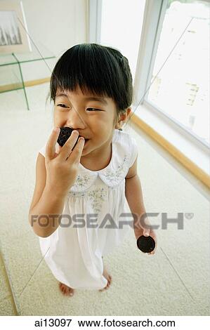 Stock Photo - Little girl eating cookie, high angle view. Fotosearch