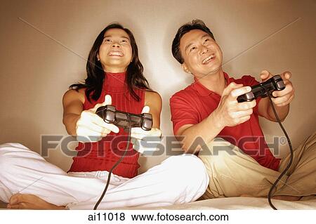 Stock Photo - Man and woman playing with handheld video game, looking forward. Fotosearch
