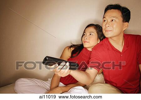 Man and woman sitting side by side, man holding remote control View Large Photo Image Stock Photo - Man and woman sitting side by side, man holding remote control. Fotosearch