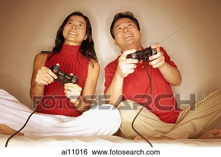Man and woman sitting side by side, legs crossed, playing with handheld video game View Large Photo Image Stock Photograph - Man and woman sitting side by side, legs crossed, playing with handheld video game. Fotosearch