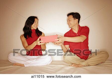 Stock Photography - Man and woman sitting side by side, legs crossed, holding a box between them.. Fotosearch