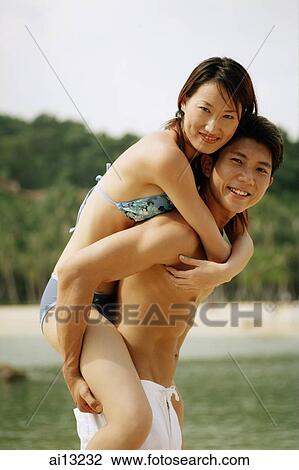Stock Image - Man carrying woman on back, both looking at camera. Fotosearch
