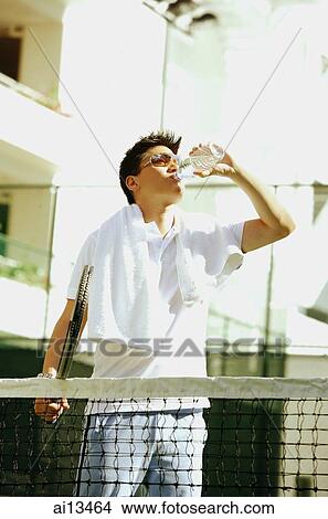Man drinking from water bottle, holding tennis racket View Large Photo Image Picture - Man drinking from water bottle, holding tennis racket. Fotosearch