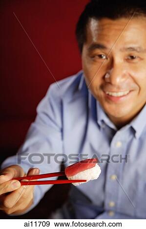 Man holding sushi with chopsticks View Large Photo Image Stock Photo - Man holding sushi with chopsticks. Fotosearch