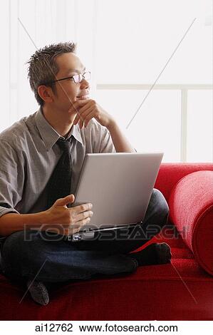 Man in shirt and tie, sitting on sofa, using laptop, looking away View Large Photo Image Stock Image - Man in shirt and tie, sitting on sofa, using laptop, looking away. Fotosearch