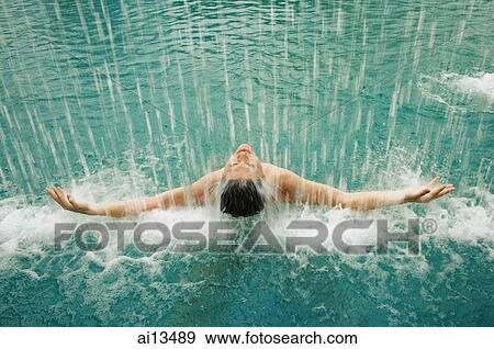 Stock Photo - Man in swimming pool, water cascading over him. Fotosearch