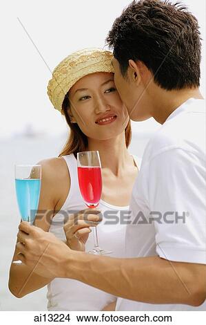 Man kissing woman, holding cocktails View Large Photo Image Picture - Man kissing woman, holding cocktails. Fotosearch