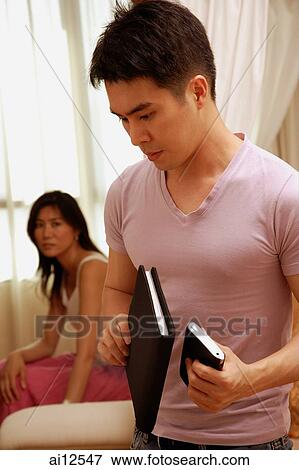 Man looking down, holding notebook and PDA, woman in background View Large Photo Image Stock Photo - Man looking down, holding notebook and PDA, woman in background. Fotosearch