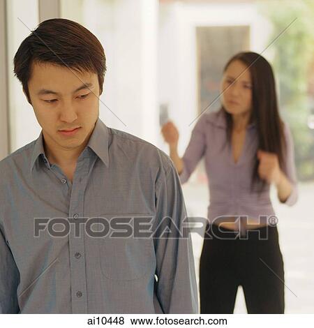 Man looking down, woman behind him gesturing View Large Photo Image Stock Photo - Man looking down, woman behind him gesturing. Fotosearch