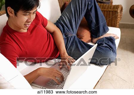 Man lying on sofa, using laptop View Large Photo Image Stock Image - Man lying on sofa, using laptop. Fotosearch