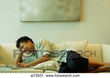 Man lying on sofa, using laptop View Large Photo Image Stock Image - Man lying on sofa, using laptop. Fotosearch