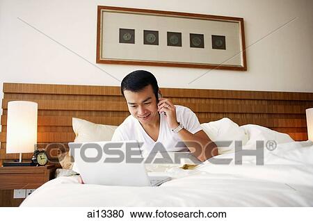 Man on bed using laptop and mobile phone View Large Photo Image Stock Image - Man on bed using laptop and mobile phone. Fotosearch