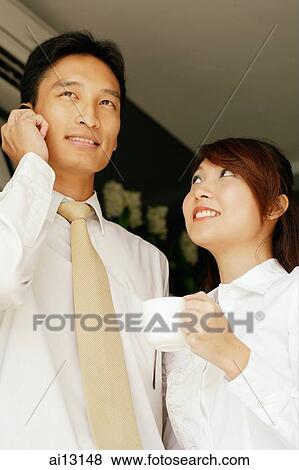 Man on mobile phone, woman holding cup, next to him View Large Photo Image Stock Photo - Man on mobile phone, woman holding cup, next to him. Fotosearch
