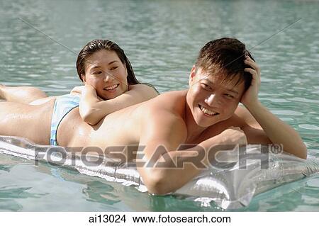 Picture - Man on pool raft, woman leaning on man. Fotosearch