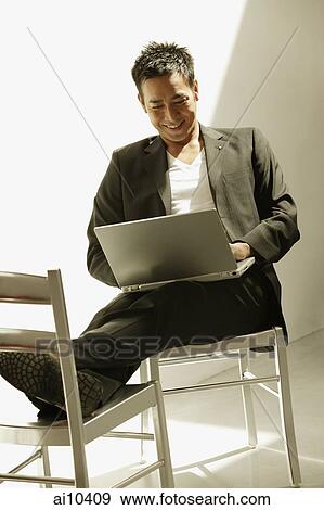 Man sitting down, using laptop, feet up on chair View Large Photo Image Stock Photo - Man sitting down, using laptop, feet up on chair. Fotosearch