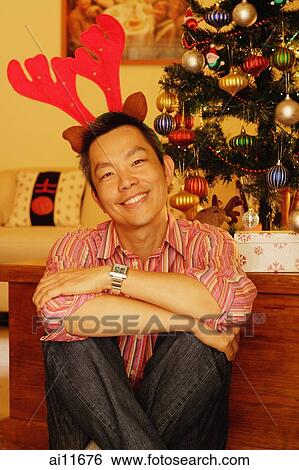 Man sitting next to Christmas tree, wearing reindeer antlers View Large Photo Image Stock Photograph - Man sitting next to Christmas tree, wearing reindeer antlers. Fotosearch