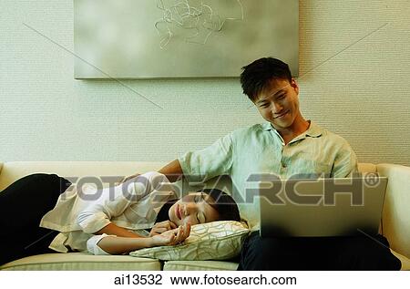 Man sitting on sofa, using laptop, woman lying next to him View Large Photo Image Stock Image - Man sitting on sofa, using laptop, woman lying next to him. Fotosearch