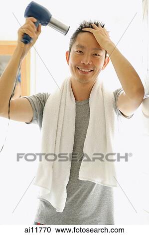Stock Image - Man using hair dryer, looking at camera. Fotosearch