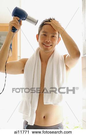 Stock Image - Man using hair dryer, looking at camera, towel around neck. Fotosearch