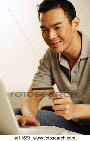 Stock Image - Man using laptop, holding credit card. Fotosearch