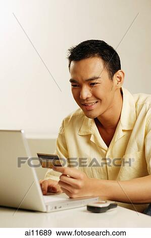Stock Photo - Man using laptop, holding credit card. Fotosearch