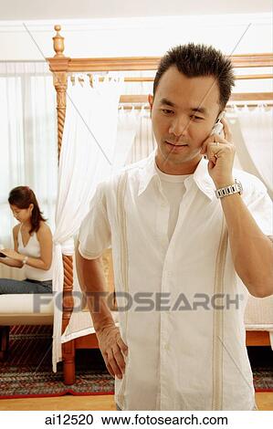 Man using mobile phone, hand on hip, woman in background reading View Large Photo Image Stock Image - Man using mobile phone, hand on hip, woman in background reading. Fotosearch