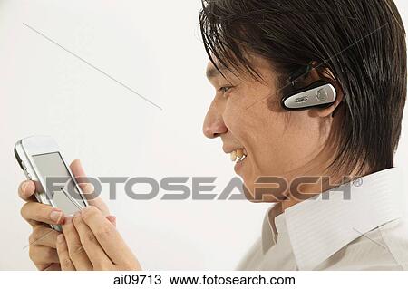 Stock Image - Man using PDA, smiling. Fotosearch