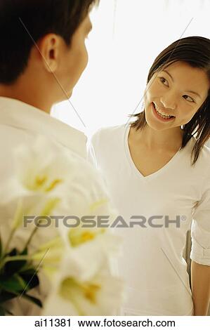 Man with flowers behind his back, woman looking at him, smiling View Large Photo Image Stock Image - Man with flowers behind his back, woman looking at him, smiling. Fotosearch