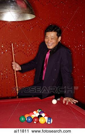 Stock Image - Man with pool cue leaning on table.. Fotosearch