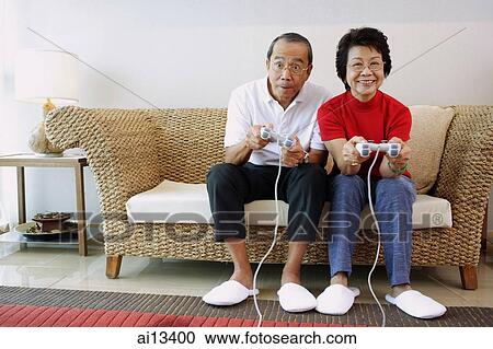 Mature couple sitting on sofa playing video games View Large Photo Image Stock Image - Mature couple sitting on sofa playing video games. Fotosearch