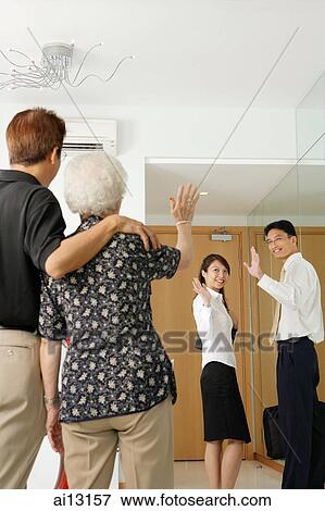 Stock Photo - Mature man and woman waving, younger man and woman waving back. Fotosearch