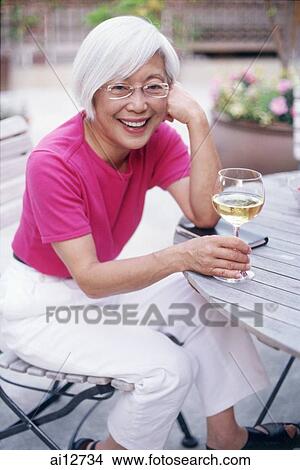 Mature woman sitting outdoors with wine glass, looking at camera View Large Photo Image Picture - Mature woman sitting outdoors with wine glass, looking at camera. Fotosearch