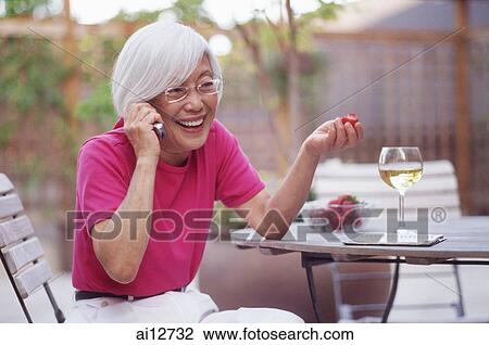 Stock Image - Mature woman using mobile phone, smiling. Fotosearch