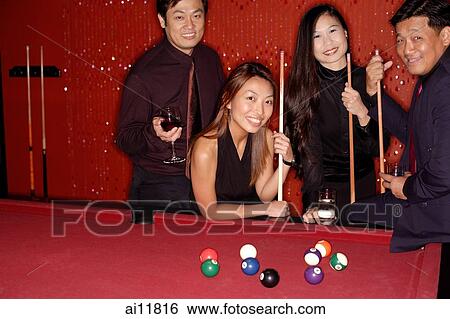 Stock Photograph - Men and women standing around pool table, looking at camera. Fotosearch