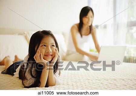 Stock Photography - Mother and daughter in bedroom, mother using laptop. Fotosearch