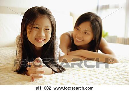 Stock Image - Mother and daughter lying on bed, smiling. Fotosearch