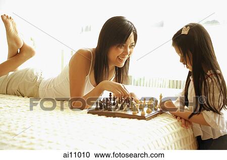 Stock Image - Mother and daughter playing chess in bedroom. Fotosearch