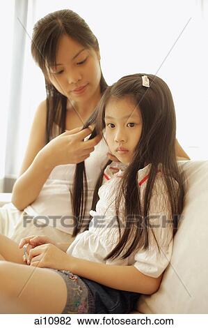 Stock Image - Mother and daughter, sitting side by side, mother braiding daughter's hair.. Fotosearch