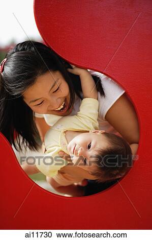 Stock Image - Mother carrying baby girl in playground. Fotosearch