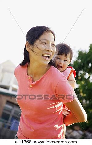 Stock Photo - Mother carrying baby girl on her back, laughing. Fotosearch