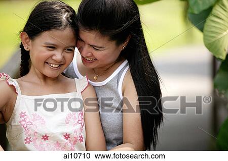 Stock Image - Mother hugging daughter, smiling. Fotosearch