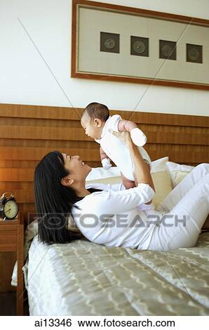 Mother lying on bed, lifting baby girl View Large Photo Image Stock Photograph - Mother lying on bed, lifting baby girl. Fotosearch