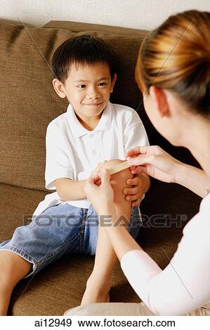 Stock Photo - Mother putting bandage on son's knee. Fotosearch