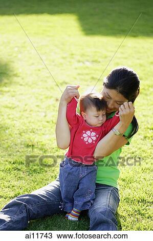 Mother sitting on lawn, holding baby girl View Large Photo Image Stock Image - Mother sitting on lawn, holding baby girl. Fotosearch