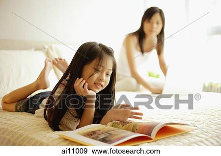 Stock Photo - Mother using laptop, daughter flipping through book. Fotosearch